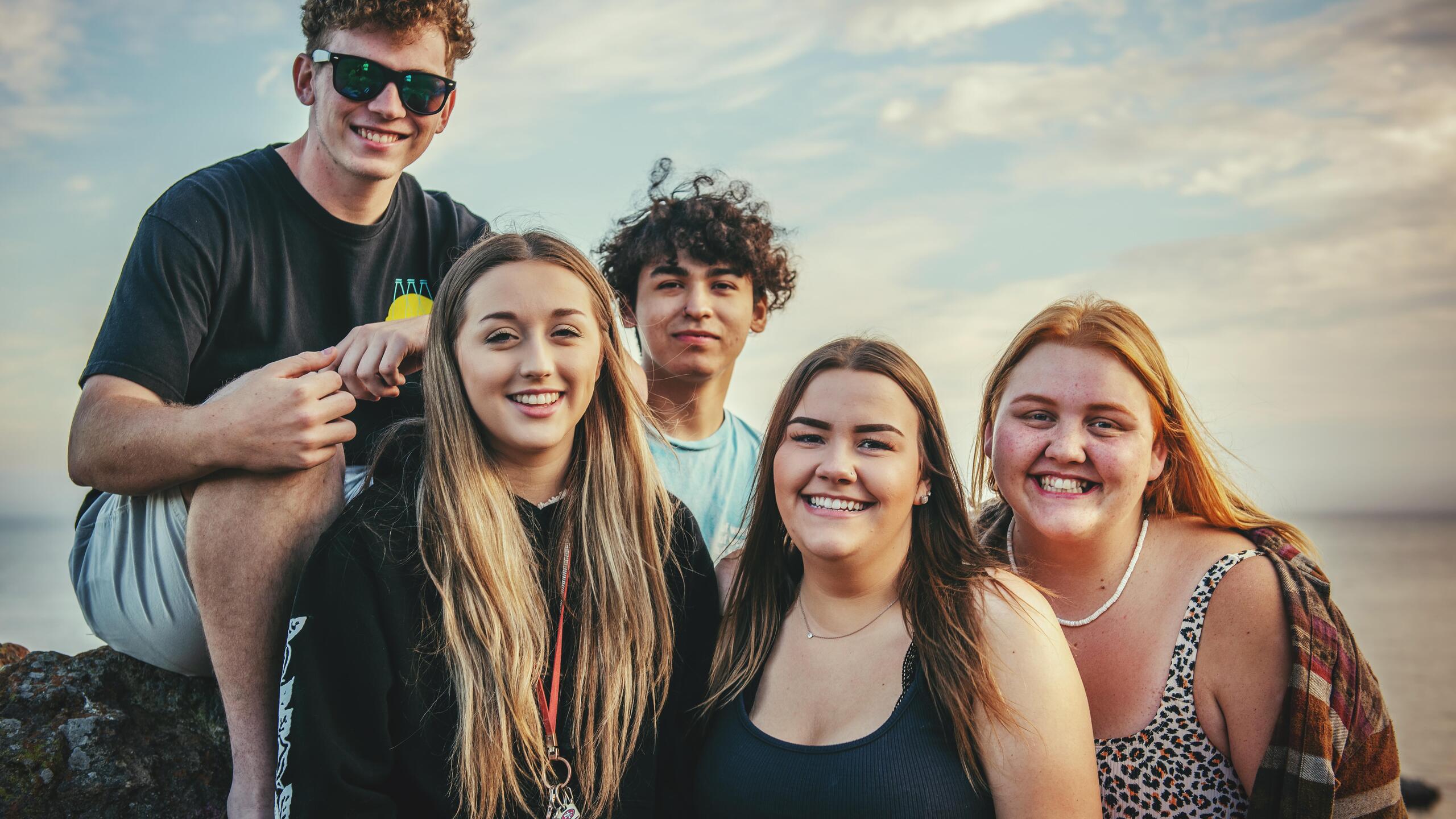 Gruppe junger lachender Menschen vor dem Meer und einem Fels