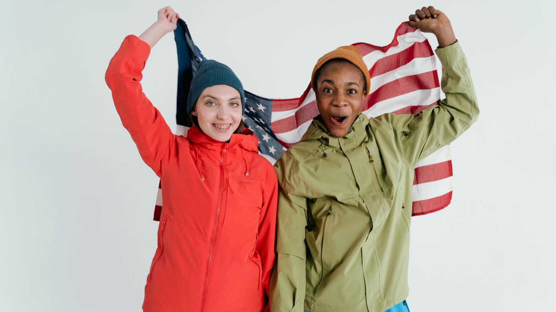 2 Jugendliche mit USA Flagge gekleidet in roter und grüner Jacke und Mützen