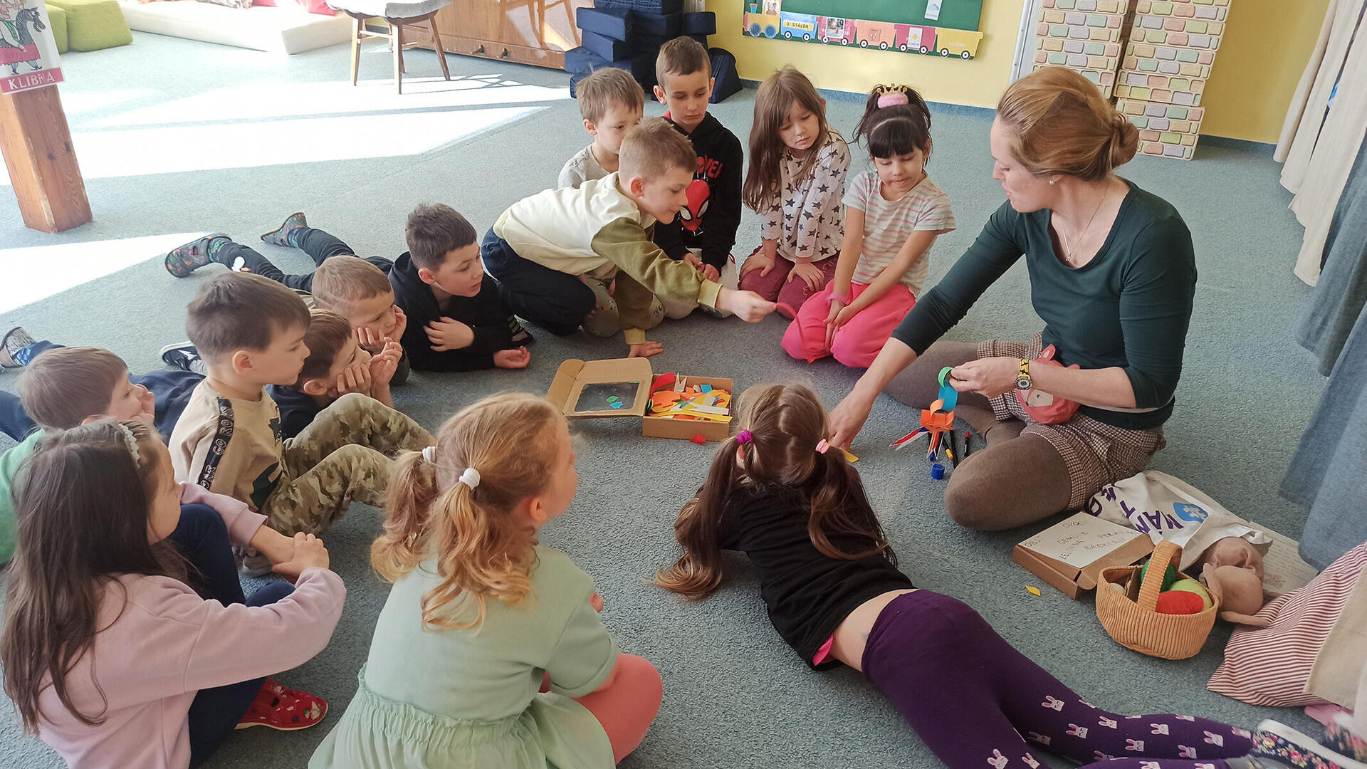 Sprachanimateurin sitzt in einem Kreis mit Kindergartenkindern und bringt ihnen neue Worte in der Fremdsprache bei