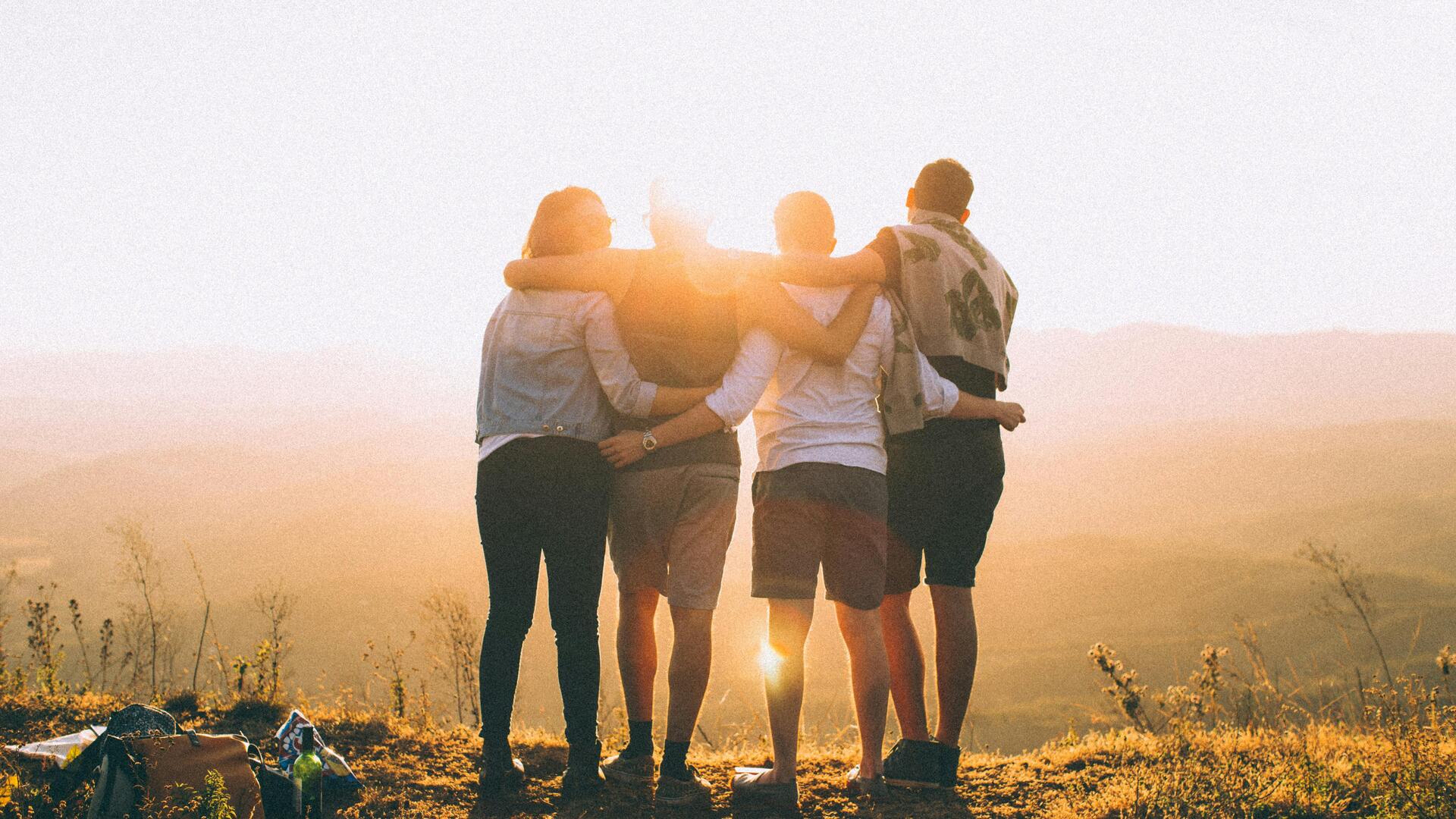 4 Jugendliche stehen vor Sonnenuntergang Arm in Arm