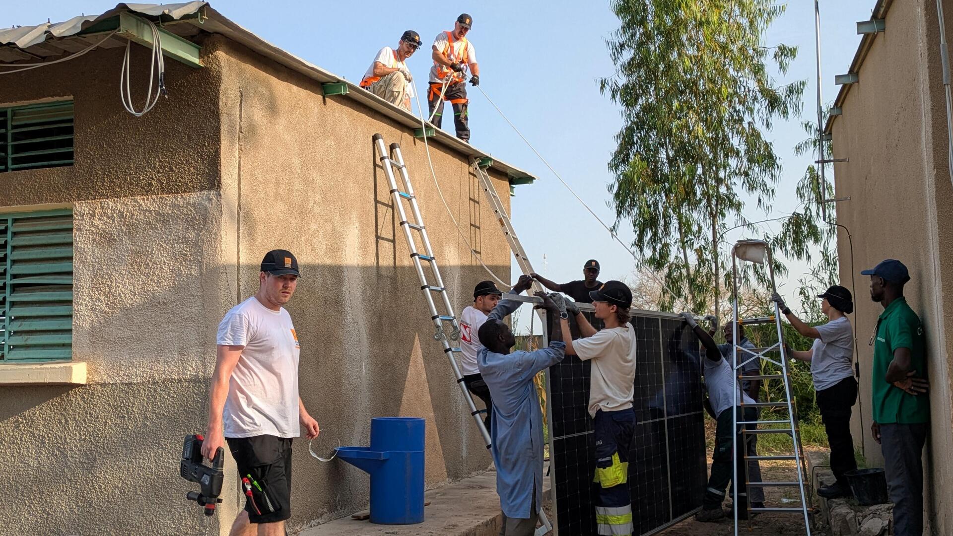 Europäische und afrikanische Auszubildende aus Nürnberg befestigen eine Solaranlage auf dem Dach einer Schule im Senegal.