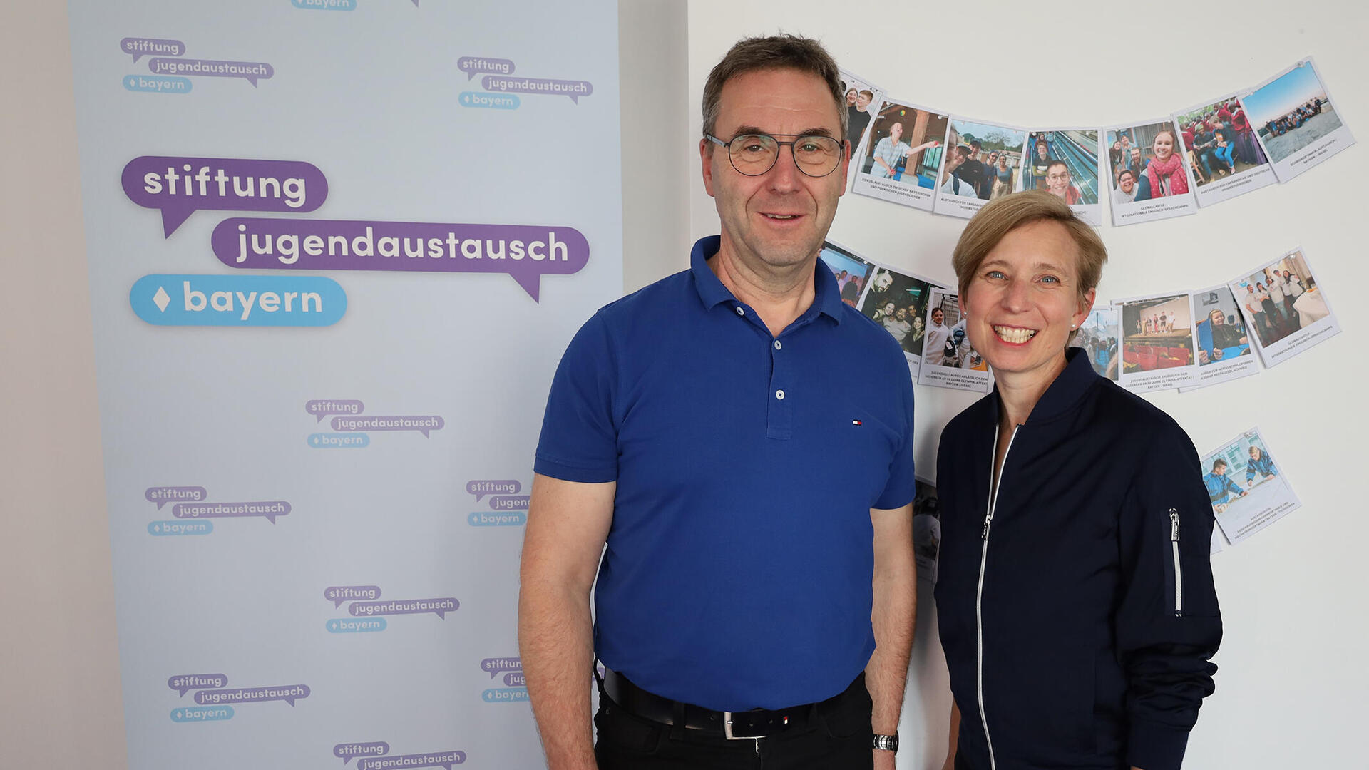 Die Geschäftsführer Wolfgang Schwarzenberger und Mirjam Eisele vor einem Banner der Stiftung Jugendaustausch Bayern
